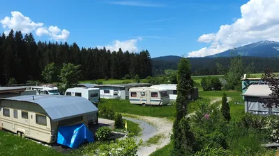 Reihe von Wohnwagen auf den Jahresplätzen, dahinter Wald und Berge