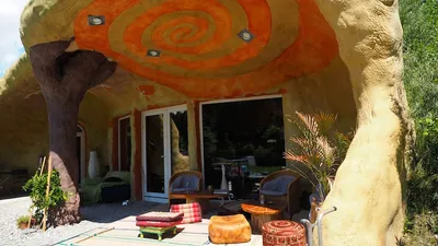 Überdachte Terrasse des Erdhauses mit oranger Spirale an der Decke, Sitzkissen und Korbsesseln