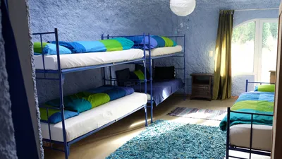 Blaues Zimmer im Erdhaus mit Etagenbetten und Einzelbett, Wandflächen in rauem Verputz