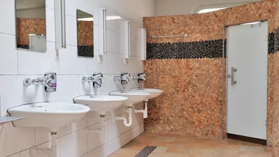 Waschraum mit vier Lavabos, Spiegeln und einer Wand aus Kieselmosaik